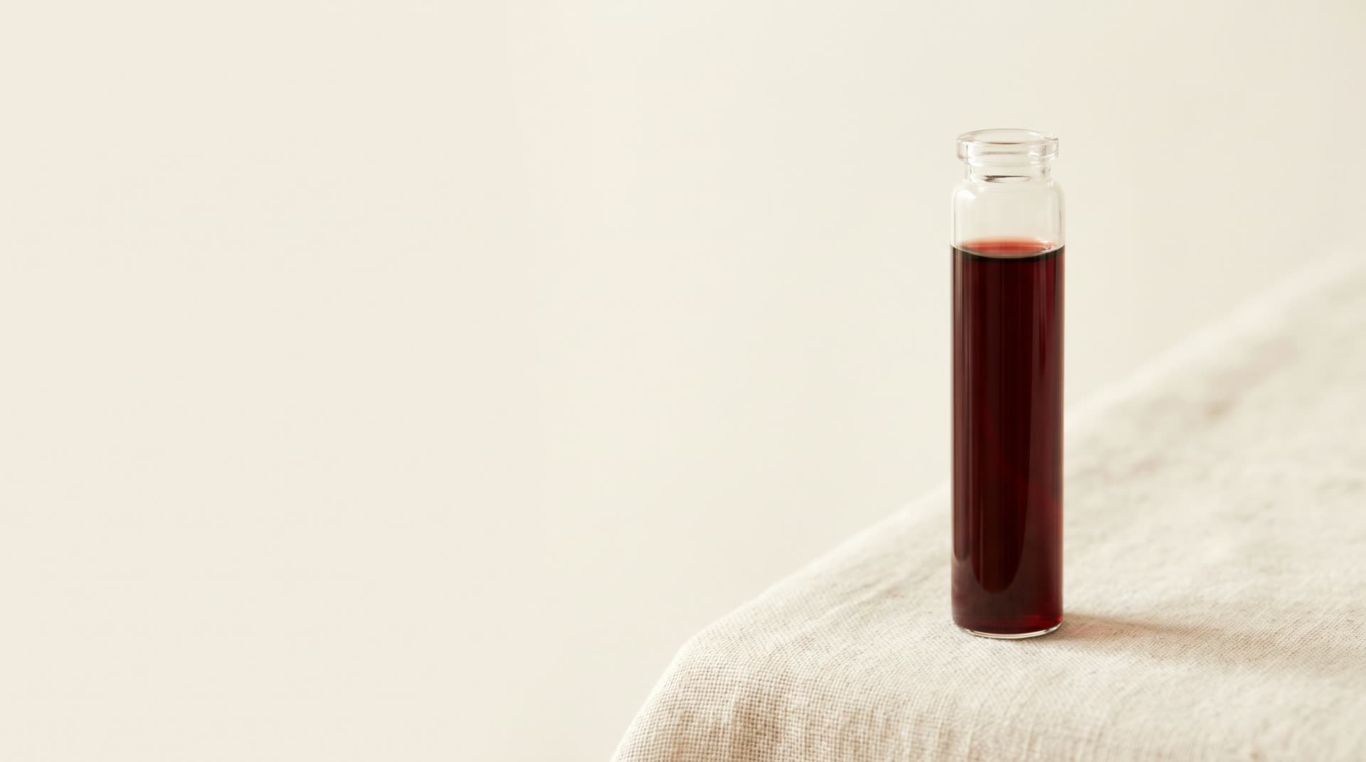 A single glass vial of deep red blood standing upright on bone linen.